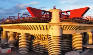 Stadion AC Milan w złotym świetle zachodzącego słońca, z charakterystycznymi czerwonymi elementami konstrukcji i betonowymi filarami.