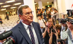 Mężczyzna w garniturze, jak kapitan reprezentacji Polski, otoczony przez fotoreporterów z aparatami.