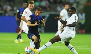 Piłkarze walczą o piłkę na boisku, jeden z nich w białej koszulce z logo Bundesligi, być może to przyszli bundesliga mistrzowie.