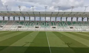 Puste trybuny stadionu RKS Radomiak Radom z napisem "RADOMIAK" ułożonym z zielonych i białych siedzeń.