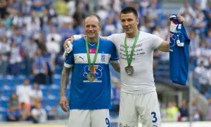 Dwóch piłkarzy z medalami na szyi, jeden z koszulką w ręku. Uśmiechnięci, świętują sukces, być może to koniec kariery.