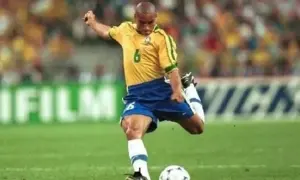 Roberto Carlos, z numerem 6 na koszulce, wykonuje potężne uderzenie piłki na boisku.