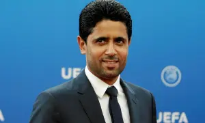 Nasser Al-Khelaifi, właściciel PSG, w eleganckim garniturze na tle niebieskiej ściany z logo UEFA.