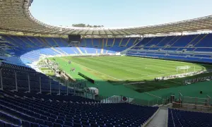 Puste trybuny stadionu Lazio, z zieloną murawą i bramkami, czekają na kibiców.
