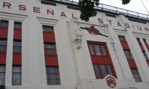 Stary stadion Arsenalu z czerwonymi oknami i napisem "ARSENAL STADIUM". Widoczny herb klubu i armata.