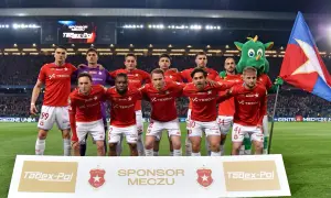 Piłkarze Wisły Kraków w czerwonych strojach, z maskotką i flagą. Najnowsze wisła kraków aktualności.
