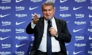 Joan Laporta, właściciel Barcelony, przemawia do mikrofonu na tle niebieskiej ściany z logo sponsorów klubu.
