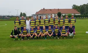 Drużyna KS Iskra Stolec gotowa do meczu. Piłkarze w żółto-niebieskich strojach, jeden w bramkarskim.