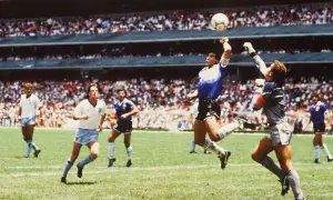Diego Maradona, w słynnym meczu, używa "ręka boga", by zdobyć bramkę. Piłkarze w białych strojach patrzą z niedowierzaniem.