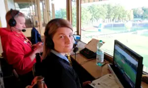 Komentator sportowy w słuchawkach przygotowuje się do transmisji. Obok monitor, mikrofon i butelka wody.