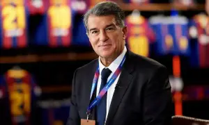 Prezes FC Barcelona, Joan Laporta, w garniturze, z identyfikatorem klubu na szyi, na tle klubowych koszulek.