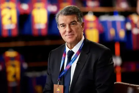 Joan Laporta, prezydent FC Barcelona, w garniturze, z identyfikatorem klubu. W tle widoczne koszulki piłkarskie.
