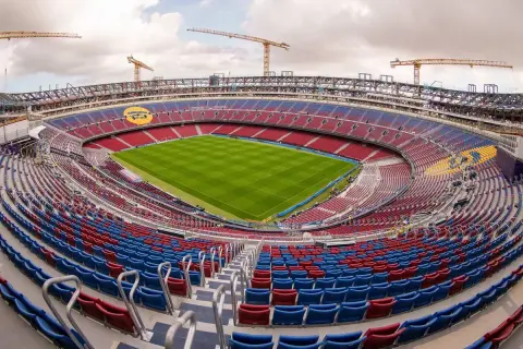 Widok na budowę nowego Camp Nou. Krany budowlane górują nad trybunami stadionu w kolorach czerwonym i niebieskim, z zieloną murawą boiska.