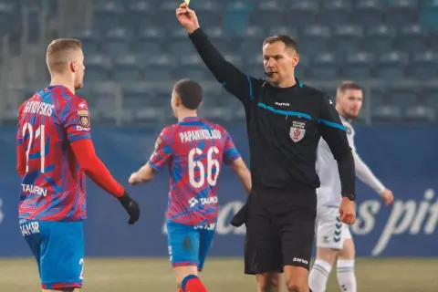 Polscy sędziowie piłkarscy w akcji. Sędzia pokazuje żółtą kartkę zawodnikowi z numerem 21.