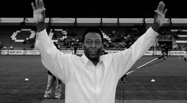 Pelé z uniesionymi rękami na tle stadionu. Jego wzrost i charyzma zawsze robiły wrażenie.