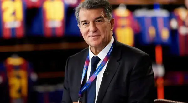 Joan Laporta, prezydent FC Barcelona, w garniturze, z identyfikatorem klubu. W tle widoczne koszulki piłkarskie.