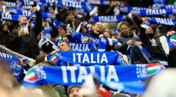 Tłum kibiców na meczu, trzymający niebieskie szaliki z napisem "ITALIA" i flagą Włoch. Emocje towarzyszące kibicowaniu podczas mistrzostw świata.
