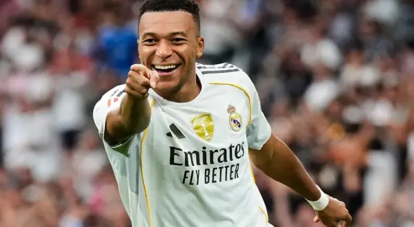 Uśmiechnięty piłkarz w białej koszulce Realu Madryt wskazuje palcem, jakby pytał: ile goli ma Mbappe?