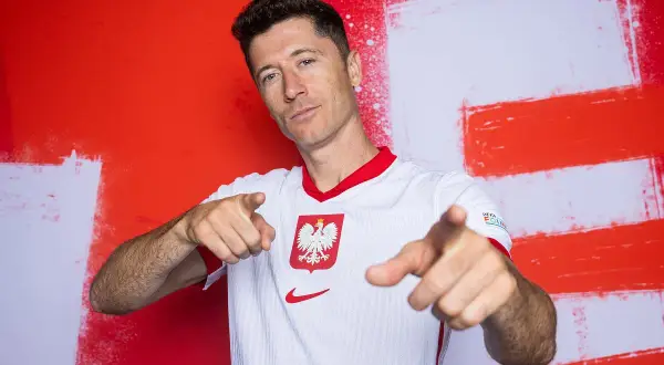 Robert Lewandowski, piłkarz roku uefa, w koszulce reprezentacji Polski, wskazuje palcami w stronę widza.