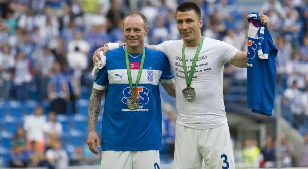 Dwóch piłkarzy z medalami na szyi, jeden z koszulką w ręku. Uśmiechnięci, świętują sukces, być może to koniec kariery.