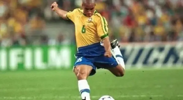 Roberto Carlos, z numerem 6 na koszulce, wykonuje potężne uderzenie piłki na boisku.