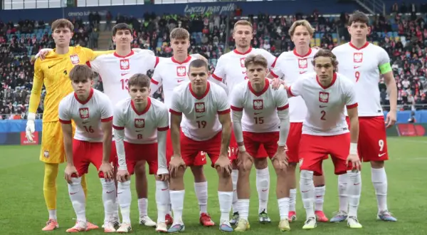 Młoda drużyna piłkarska w biało-czerwonych strojach, gotowa do gry. W tle trybuny stadionu, gdzie kibice dopingują lublin klub piłkarski.
