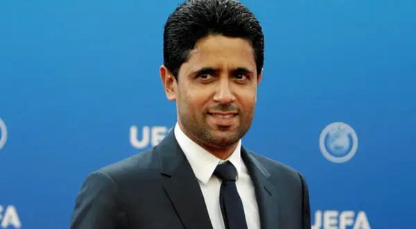 Nasser Al-Khelaifi, właściciel PSG, w eleganckim garniturze na tle niebieskiej ściany z logo UEFA.