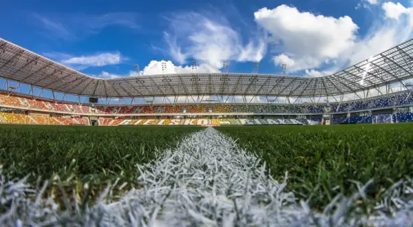 Piękny, pusty stadion Podbeskidzie z kolorowymi trybunami i zieloną murawą pod błękitnym niebem.