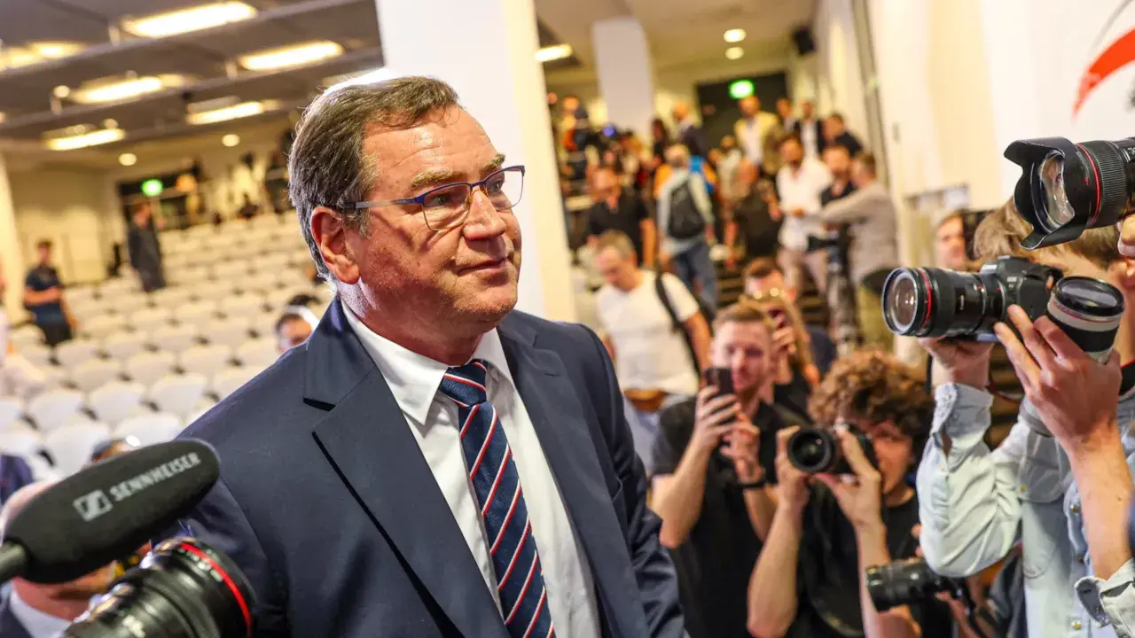 Mężczyzna w garniturze, jak kapitan reprezentacji Polski, otoczony przez fotoreporterów z aparatami.