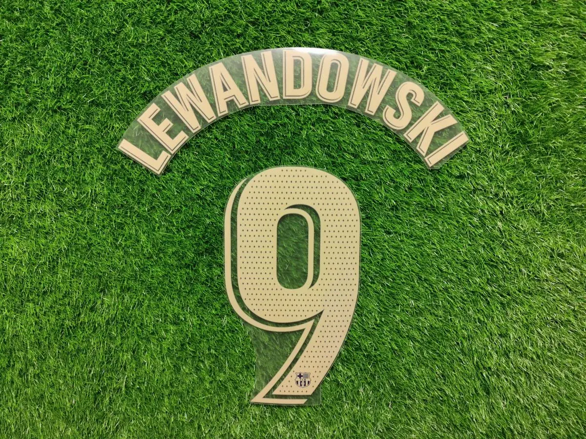 Numer 9 z nazwiskiem Lewandowski i logo Barcy na zielonej murawie.