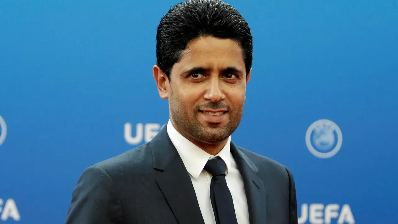 Nasser Al-Khelaifi, właściciel PSG, w eleganckim garniturze na tle niebieskiej ściany z logo UEFA.