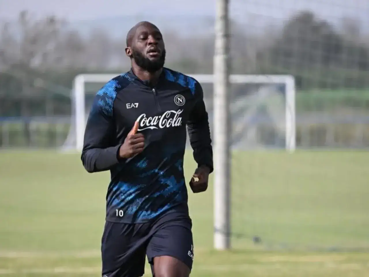 Piłkarz w czarnej koszulce z niebieskimi wzorami i numerem 10, z logo Coca-Cola, biegnie po boisku. Lukaku waga jest w świetnej formie.