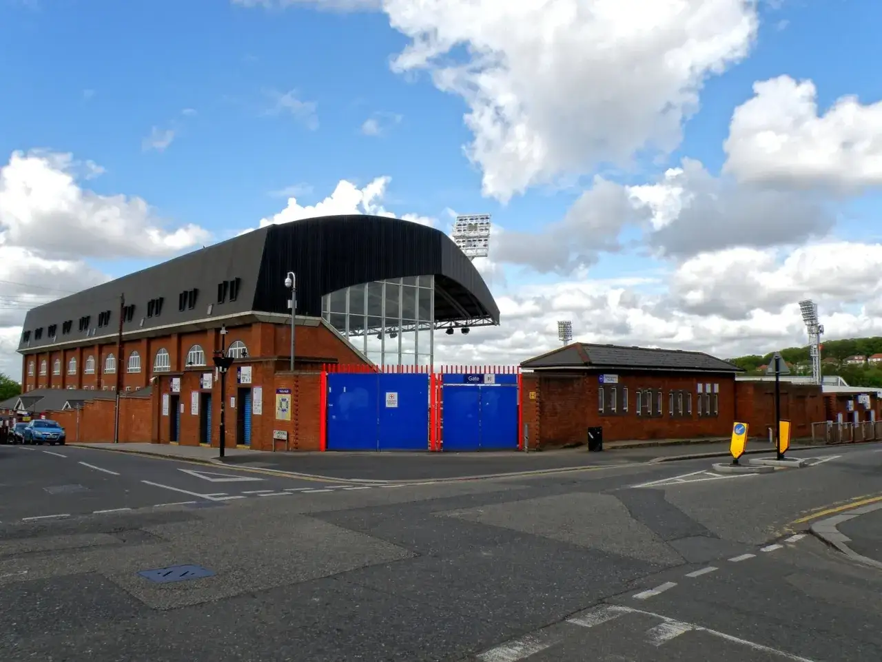 Widok na bramę stadionu Crystal Palace. Budynek z cegły z czarnym dachem i niebieskimi bramami.