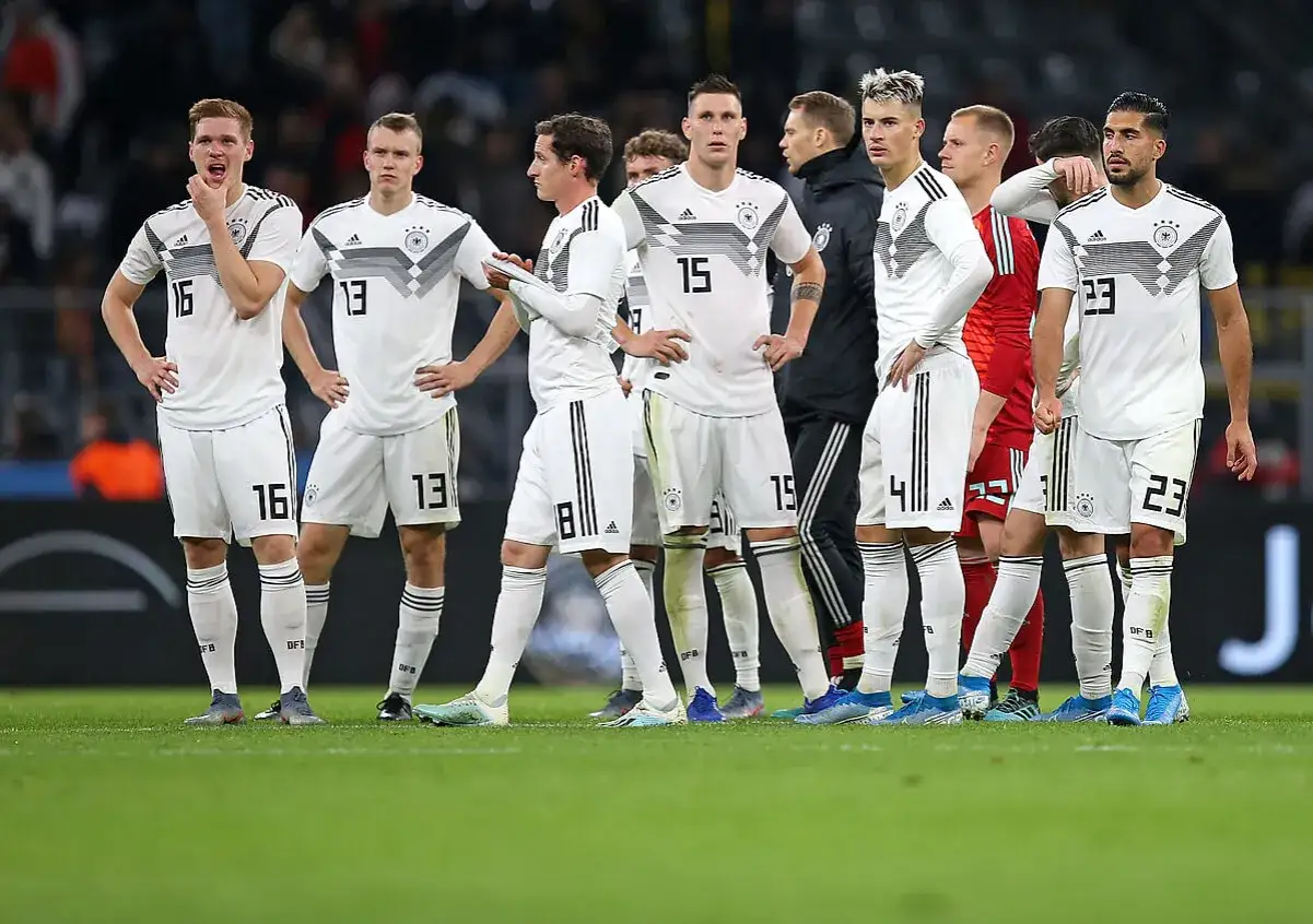 Piłkarze reprezentacji Niemcy FC w białych strojach, z numerami na koszulkach, stoją na boisku.