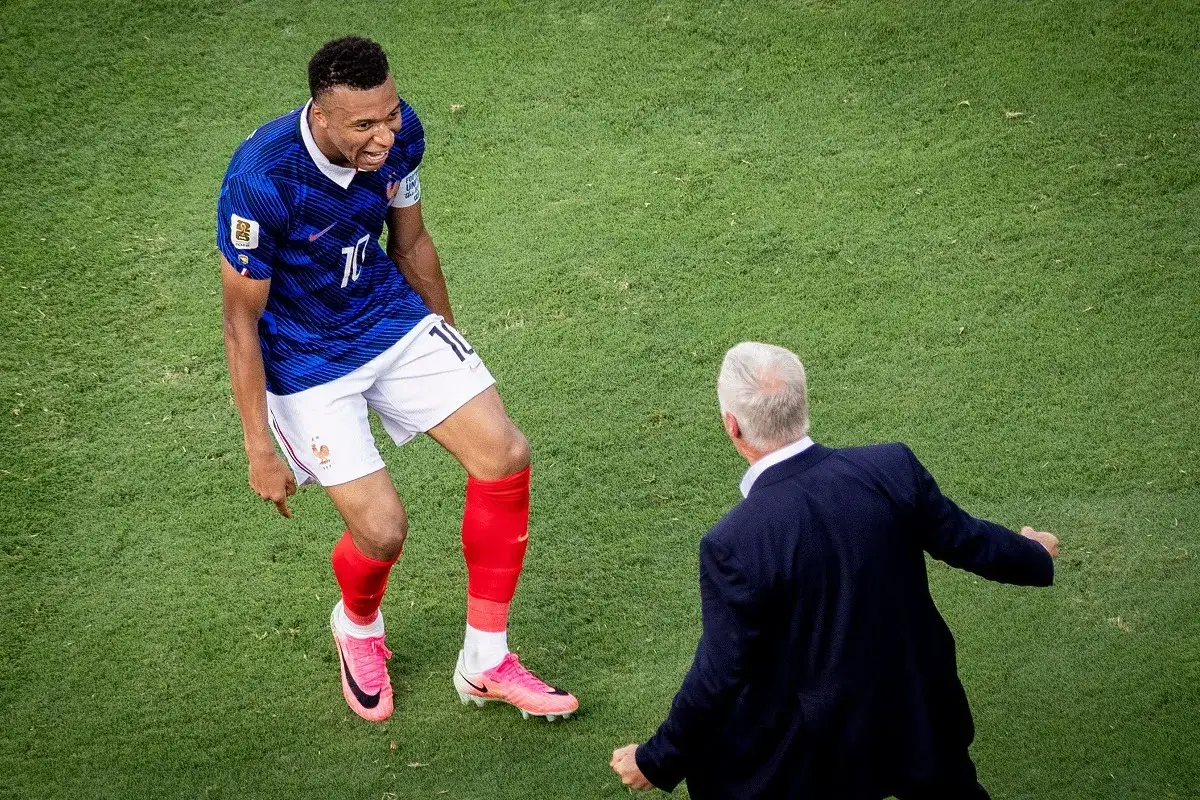 Piłkarz w niebieskiej koszulce z numerem 10 cieszy się z gola, a trener w garniturze gratuluje mu. Ile goli ma Mbappe?
