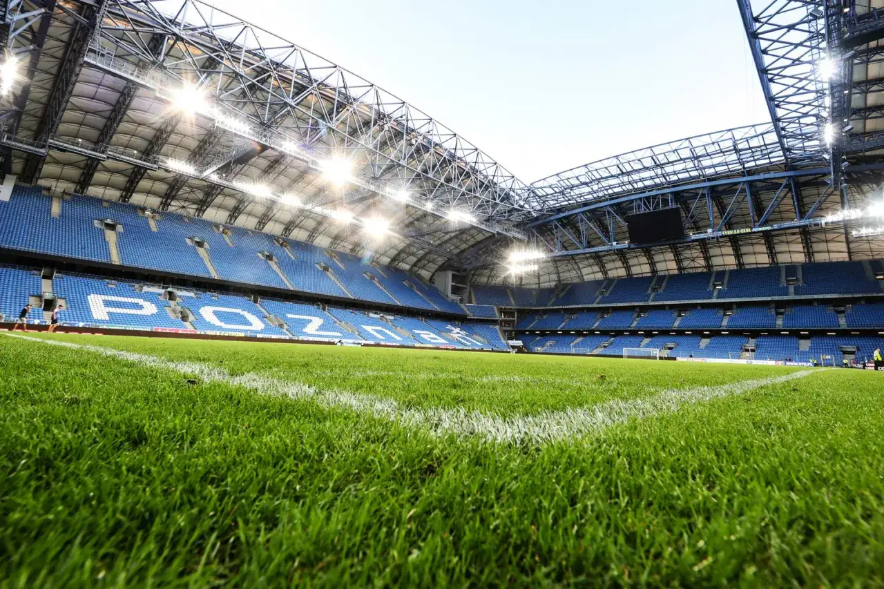 Pusta trybuna stadionu z niebieskimi siedzeniami, na których widnieje napis
