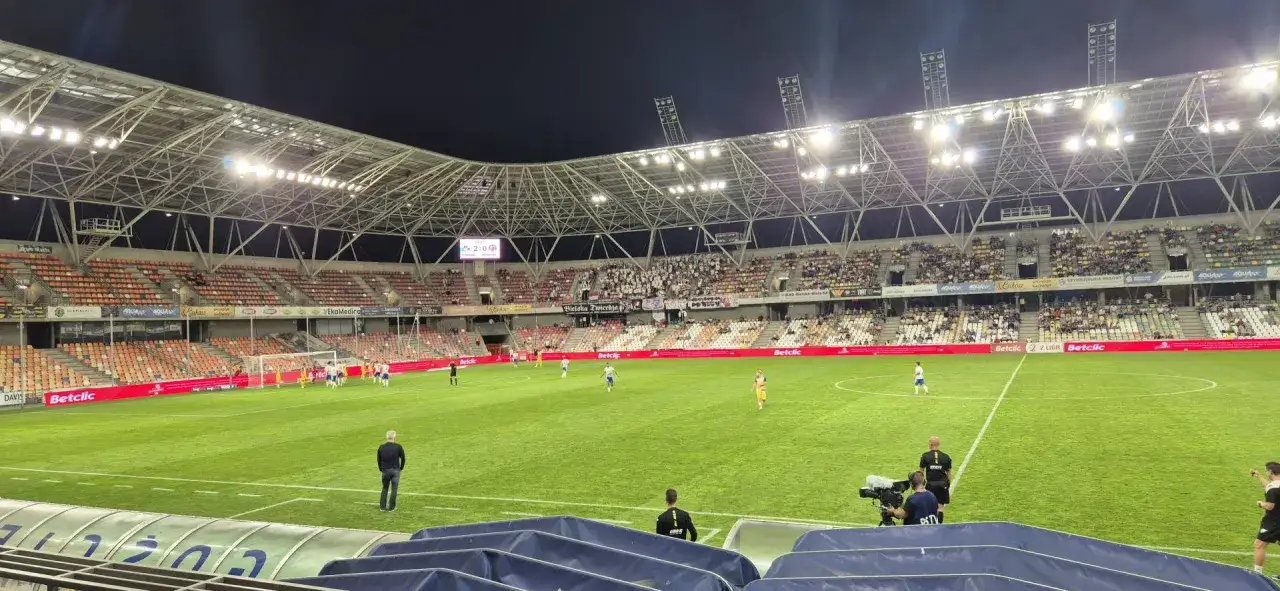 Mecz na stadionie miejskim w Bielsku-Białej. Piłkarze na zielonej murawie, trybuny częściowo wypełnione.