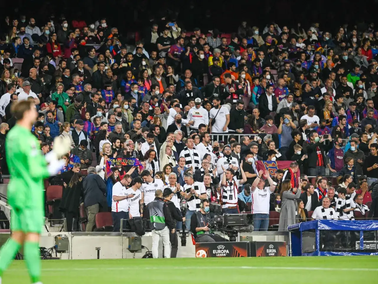 Tłum kibiców na stadionie, niektórzy w barwach FC Barcelona, inni w strojach gości. Widać transparenty z napisami