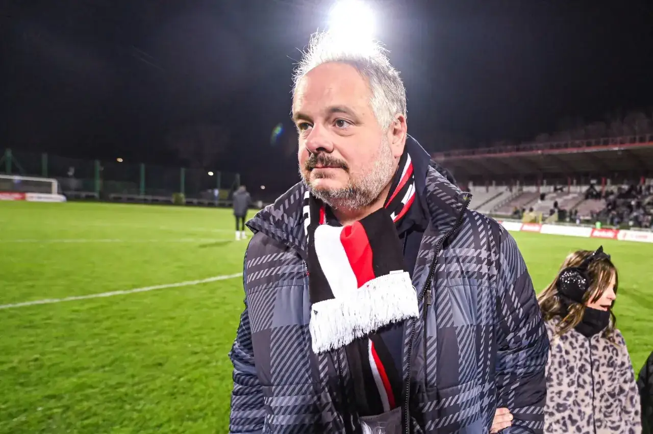 Prezes Polonii Warszawa, ubrany w klubowy szalik, obserwuje mecz na stadionie.