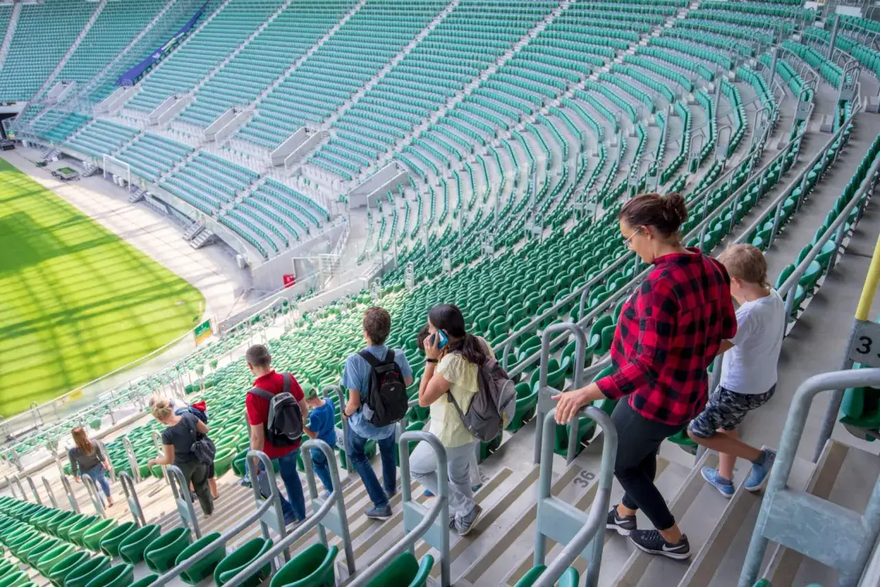 Grupa osób wchodzi na zielone trybuny stadionu. Tarczyński Arena pojemność robi wrażenie, a widzowie zajmują miejsca.