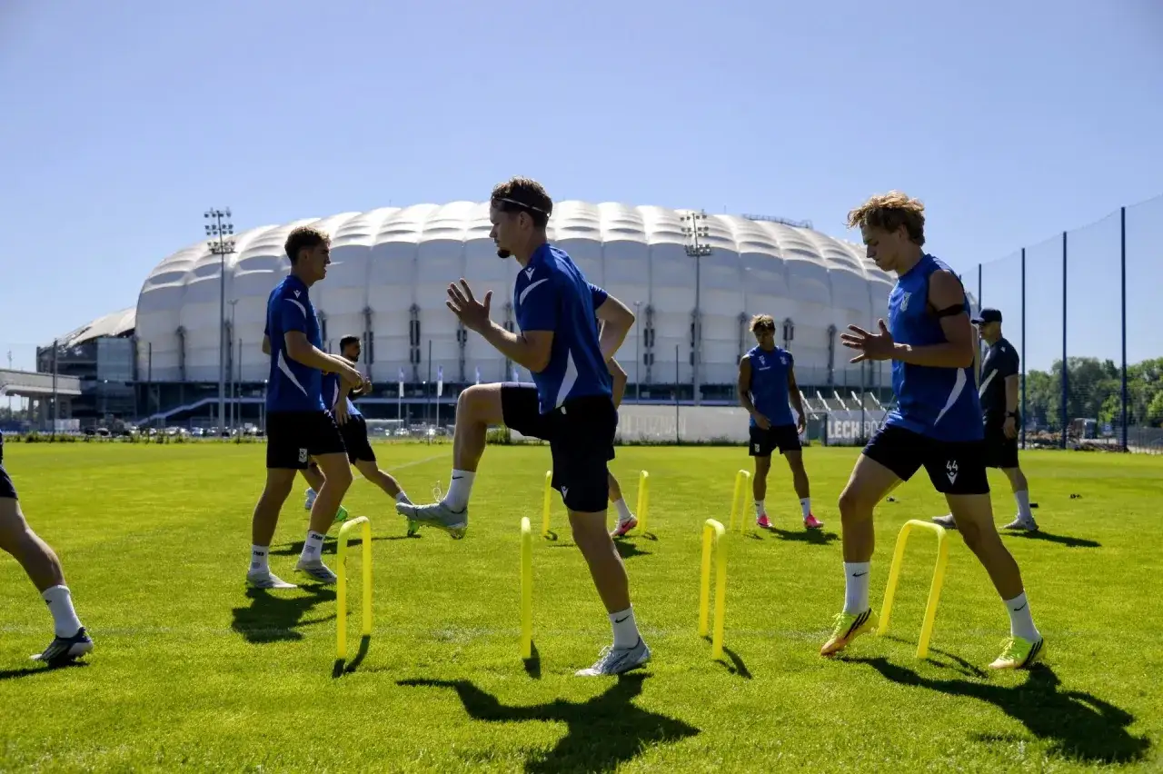 Piłkarze Lecha Poznań dzisiaj trenują na boisku przed stadionem, pokonując niskie żółte płotki.