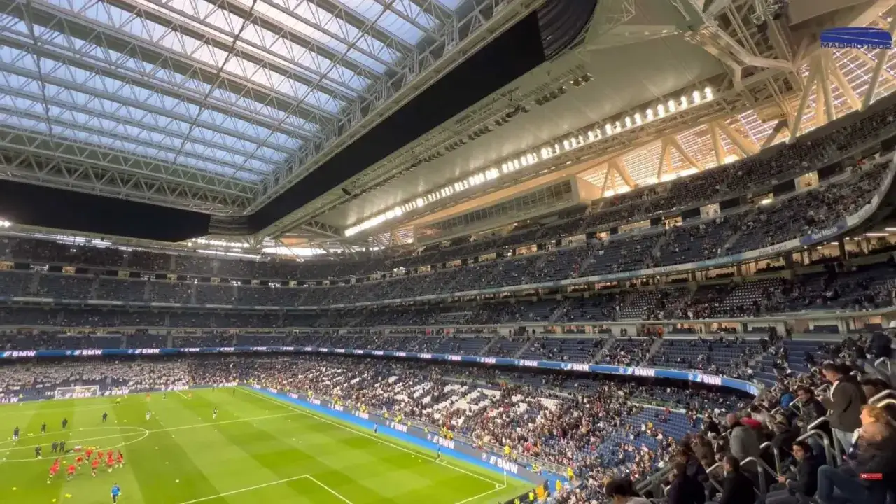 Widok na wypełniony po brzegi stadion Realu Madryt. Trybuny zapełnione kibicami, na murawie piłkarze podczas rozgrzewki.
