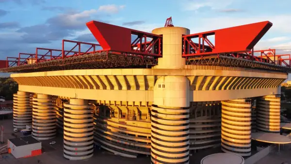 Stadion AC Milan w złotym świetle zachodzącego słońca, z charakterystycznymi czerwonymi elementami konstrukcji i betonowymi filarami.