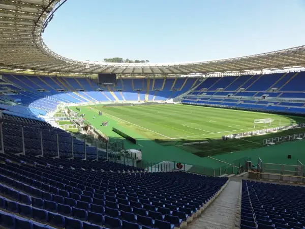 Puste trybuny stadionu Lazio, z zieloną murawą i bramkami, czekają na kibiców.