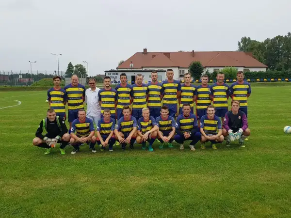 Drużyna KS Iskra Stolec gotowa do meczu. Piłkarze w żółto-niebieskich strojach, jeden w bramkarskim.